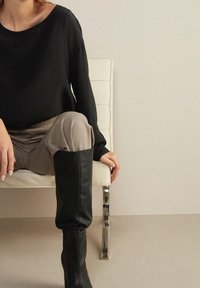 Černý top s dlouhým rukávem, měkká tkanina, volný střih; světle béžové kalhoty, hladký povrch; černé kožené boty po kolena s přiléhavým designem.