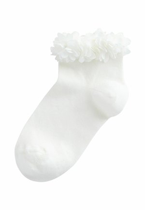 Bijela gležnjača s naboranim cvjetnim rubom oko manžete, izrađena od mekanog, rebrastog tkanja.