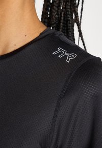 Camisa atlética negra hecha de un tejido transpirable y texturizado. Presenta un diseño ajustado con el logo de TYR en el hombro.