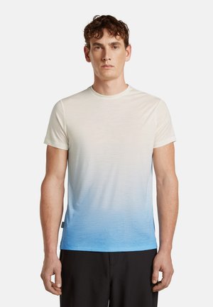 Mężczyzna stojący twarzą do przodu, ubrany w krótkim rękawem t-shirt z okrągłym dekoltem, z gradientem od białego do niebieskiego, oraz czarne spodnie.