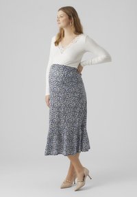 Hvit ribbet langermet topp med blonde hals, kombinert med et blått blomster-midi-skjørt med volanger i kanten. Modellen har på seg nude hæler.