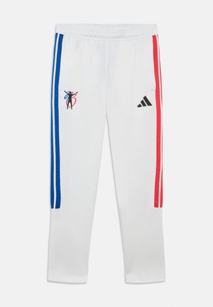 Pantalon de survêtement blanc avec des bandes latérales bleues et rouges, comportant un logo graphique et l'emblème Adidas sur la jambe gauche. Texture de tissu lisse.