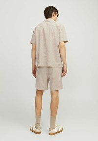 Chemise à col et manches courtes avec un short assorti en motif à carreaux beige et marron. Le tissu semble léger avec une coupe décontractée. Baskets et chaussettes visibles.