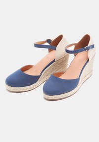 Sandali con zeppa in tessuto blu, con punta chiusa, cinturino alla caviglia e piattaforma in giuta intrecciata. Dettagli accentuati sul pannello posteriore testurizzato. Soletta in colore naturale.