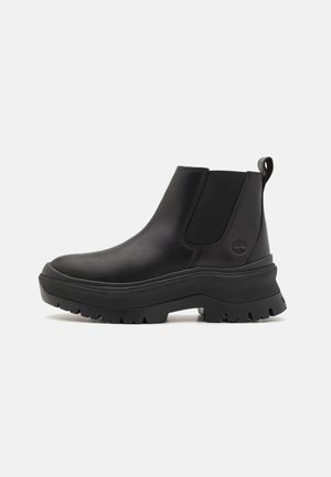 Black leather Chelsea boots with elastic side panels, chunky rubber sole, and a pull tab at the back. Features textured surface and logo detail.