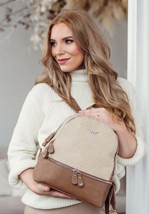 Light tan backpack with a textured upper, smooth brown lower section, and silver zippers. Accented with small leather tags and a round shape.