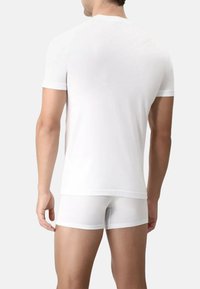 T-shirt bianca con collo a giro e maniche corte, abbinata a boxer bianchi. Tessuto liscio, design aderente senza pattern o accenti visibili.