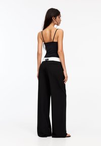 Pantaloni neri a gamba larga con una cintura bianca a contrasto, abbinati a un top nero aderente con spalline sottili. Texture del tessuto liscia.