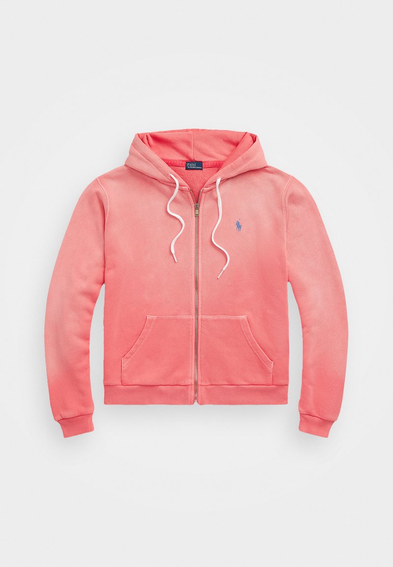 Haut zippé rose avec poches avant, cordons blancs et petit logo brodé bleu sur la poitrine gauche.