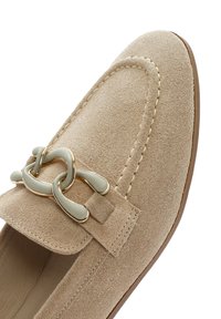 Mocassino in suede beige con punta arrotondata, hardware decorativo in oro e grigio e cuciture a contrasto lungo la cucitura. Design con suola piatta.