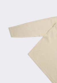 Maglione beige lavorato a maglia oversize con maniche lunghe, polsini a costine e una texture liscia, mostrato disteso su uno sfondo chiaro.