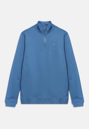 Pull bleu à fermeture éclair jusqu'au quart, manches longues, poignets et ourlet côtelés, et petit logo brodé sur la poitrine gauche.