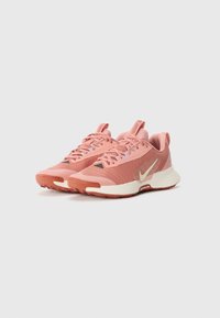 Des chaussures de sport couleur rose clair présentent un dessus en maille texturée, une semelle intermédiaire de couleur crème et une semelle en caoutchouc avec des motifs de traction visibles.