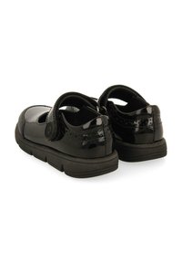 Zapatos de charol negros con punta redonda y una correa de velcro. Presentan acentos de diseño perforado y una suela de goma texturizada para mayor tracción.