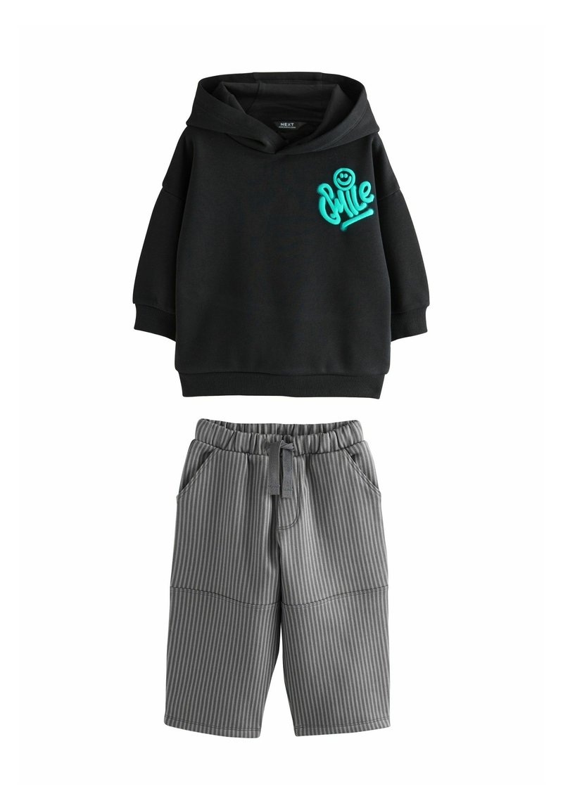 Sort hættejakke med turkise "Chill" grafik, oversized pasform, parret med grå stribede shorts med lommer og elastisk talje.