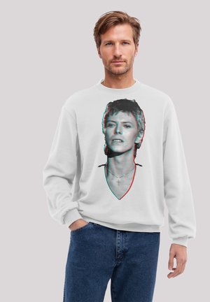 Weißes Sweatshirt mit einer stilisierten Grafik eines Kopfes in 3D-Effekt, kombiniert mit dunkelblauen Jeans. Lässiger Schnitt und weiche Textur.
