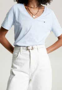 Světle modré bavlněné tričko s výstřihem do V a krátkými rukávy, zkombinované s bílými džíny s vysokým pasem a stříbrným řetízkem.