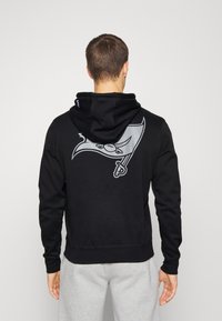 Felpa nera con logo grigio raffigurante un uccello stilizzato sul retro. Maniche lunghe, orlo a coste e cappuccio regolabile con cordino.