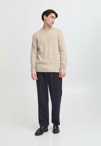Suéter de lana beige con cuello redondo, textura acabada y bajo acanalado, combinado con pantalones de corte holgado en color navy y zapatos negros.