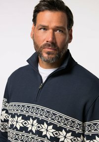 Námořnický pulovr na zip s krémovým vzorem sněhových vloček na hrudi. Hladký úplet, středně těžká tkanina a malý kovový zip jako akcent.