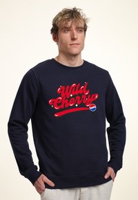 Felpa blu navy in cotone, con un audace testo grafico rosso "Wild Cherry" con accenti lucidi e un logo circolare. Maniche lunghe.