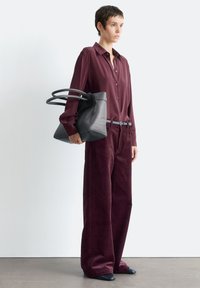Burgundy corduroy wide-leg pants, button-down burgundy shirt, black leather bag with dual handles, and dark pointed shoes.