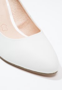Chaussure plate en cuir blanc à bout pointu, montrant une doublure intérieure texturée beige et une semelle avec un tampon de qualité du cuir.