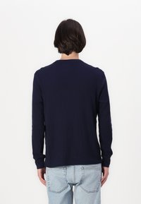 Chemise à manches longues bleu marine en texture côtelée avec un col rond, associée à un jean bleu clair ; vue de dos.