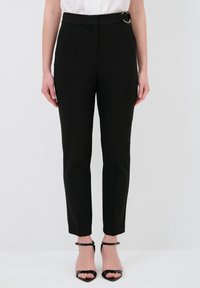 Zwarte op maat gemaakte broek met een strak ontwerp, voorzien van een ronde gouden hardwareaccent op de taille en taps toelopende broekspijpen. GLadde stoffen structuur.