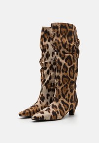 Bottes genoux en imprimé léopard, design ample, bout pointu, tissu doux, petit talon carré, motifs marron et noir prononcés.