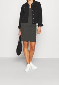 Veste en denim noir, robe ajustée grise, baskets blanches et sac tressé noir. La tenue présente un design épuré et des textures subtiles.
