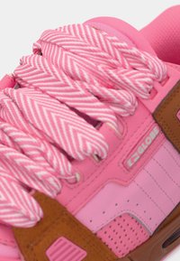 Κοντινό πλάνο ροζ αθλητικού παπουτσιού με χοντρές κορδόνια σε σχέδιο ζικ-ζακ ροζ και λευκές και καφέ λεπτομέρειες, με το λογότυπο της μάρκας Globe.