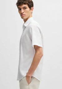 Camicia bianca a maniche corte con bottoni, dal tessuto morbido e colletto classico. Presenta dettagli di cucitura sottili e una vestibilità rilassata.