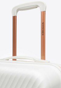 Weißer Hartschalenkoffer mit strukturierter Oberfläche, ausgestattet mit einem kupferfarbenen Teleskopgriff und einem weißen Tragegriff.