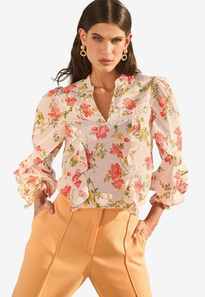 Floral blouse with ruffled sleeves, featuring pink and orange blooms on a white background. Paired with high-waisted, light orange trousers.
