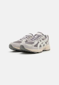 Scarpe sportive grigio chiaro con parte superiore in rete, sovrapposizioni sintetiche e suola in gomma testurizzata, con dettagli bianchi lungo i lati.