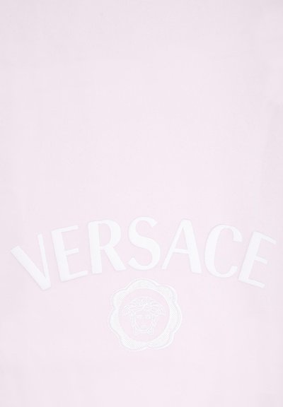 Jasnoróżowa koszulka z wytłoczonym białym napisem "VERSACE" oraz okrągłym emblematem głowy, wykonana z miękkiego materiału o gładkiej fakturze.