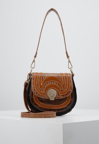 Brązowa i czarna torebka z ekoskóry z zakrzywionymi przeszyciami i złotymi elementami metalowymi. Posiada pasek na ramię oraz zapięcie na klapkę z metalowym zapięciem.