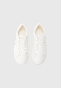 Ζευγάρι λευκά χαμηλά αθλητικά παπούτσια με κορδόνια, που βλέπουν προς τα εμπρός, σε απλό ανοιχτό γκρι φόντο.