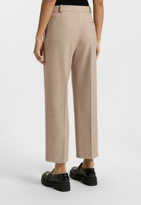 Beige wijde broek met een gestructureerde afwerking, voorzien van riemlussen en achterzakken, gedragen met zwarte plateau schoenen.