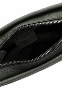 Zelená kožená taška uvnitř s uzávěrem na zip. Texturovaný povrch, minimalistický design, s označením a černým zipem.