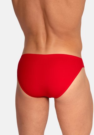 Männlicher Torso und obere Beine von hinten, bekleidet mit leuchtend roten Badehosen vor einem schlichten hellen Hintergrund.