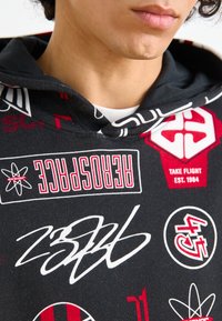 Felpa nera con grafiche rosse e bianche, caratterizzata da vari loghi e design, tra cui una grande firma. Tessuto morbido.