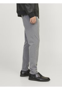 Pantalon gris ajusté avec une texture lisse, coupe slim, et poches latérales, associé à des chaussures en cuir noires au profil bas.
