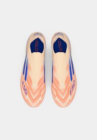 Zapatillas de fútbol ligeras y rosas sin cordones con patrones de chevrones azules y naranjas y texto "F50" sobre un fondo blanco.
