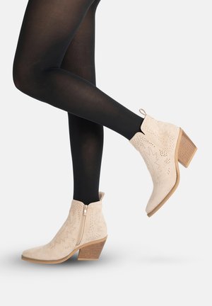 Jambes portant des collants noirs et des bottines en daim beige avec des motifs d'étoiles perforés et des talons en bois empilés.