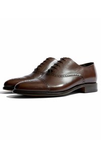 Un paio di eleganti scarpe Oxford in pelle marrone lucida con dettagli brogue e lacci neri su uno sfondo bianco.