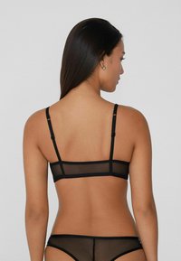Czarny siateczkowy biustonosz typu bralette z regulowanymi ramiączkami, posiadający przezroczysty design i minimalistyczną strukturę. Tylna część ma kontrastowe solidne linie.