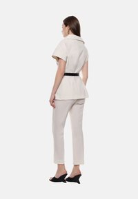 Top peplum e pantaloni sartoriali in tessuto crema, con cintura nera. Indossati con mules con tacco nere, mostrando una vestibilità elegante e linee pulite.