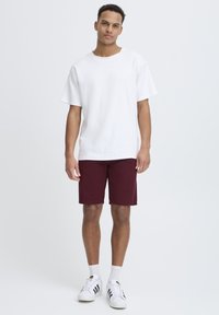 T-shirt en coton blanc, coupe ample, manches courtes ; shorts bordeaux, longueur genou ; baskets blanches avec des rayures noires ; design simple, sans motifs.